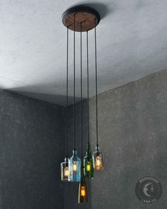 three glass bottles are hanging from a ceiling light in a room with grey walls and concrete flooring