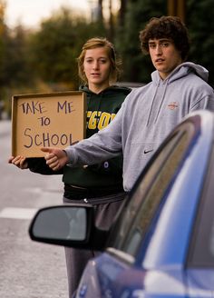 two people standing next to each other holding a sign that says take me to school