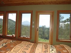 a bed sitting in a bedroom next to three windows with mountains in the background on each side