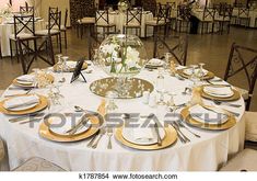 a table set up for an event with white and gold plates, silverware and napkins