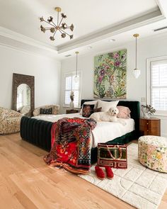 a bedroom with white walls and wooden floors has a large bed, two chairs, rugs, and artwork on the wall