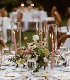 the table is set with candles, flowers and glass vases for centerpieces