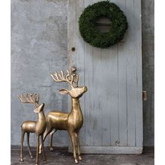 two brass deer statues in front of a door with a wreath on it's side