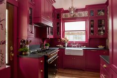 the kitchen is painted bright pink and has red cabinetry with gold trimmings