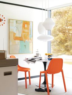 two orange chairs sit at a table in front of a large window with an abstract painting on the wall