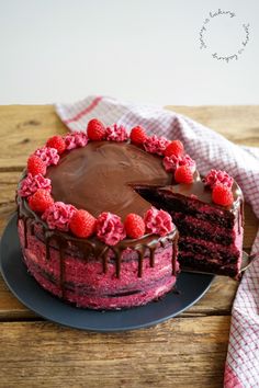 a chocolate cake with raspberries on top and one slice missing from the cake