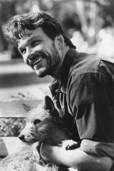 black and white photograph of a man holding a dog in his lap, smiling at the camera