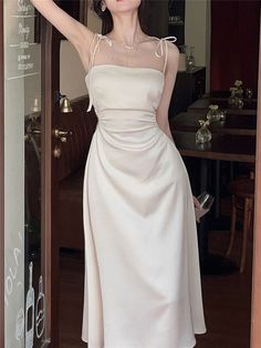 a woman standing in front of a glass door wearing a white dress with sheer shoulders