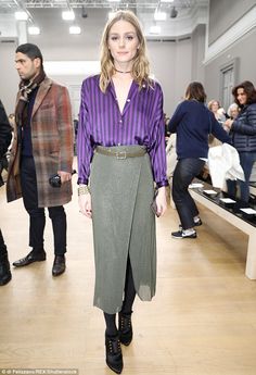 a woman in a purple shirt and green skirt standing on a wooden floor next to other people