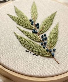 a close up of a embroidery on a wooden hoop with blue berries and green leaves