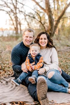 a man, woman and child are sitting on a blanket in the woods with leaves