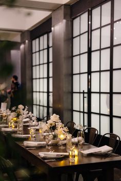 a long table is set with white flowers and candles for an elegant wedding reception in front of large windows