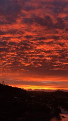 the sky is red and orange as it sets over some hills with houses in the distance