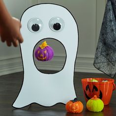 a child's hand reaching for a toy in front of a fake ghost and two pumpkins