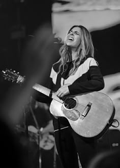 a woman singing into a microphone while holding a guitar