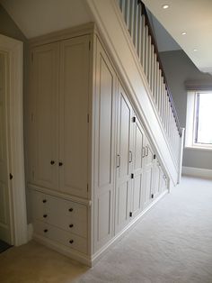 an empty room with white cabinets and drawers under the stair case next to a window