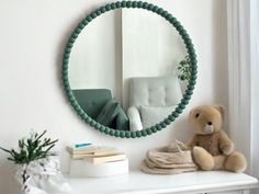 a teddy bear sitting on a white dresser next to a round mirror and green chair