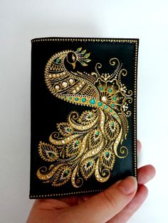 a hand holding a black wallet with gold and green designs on it's side