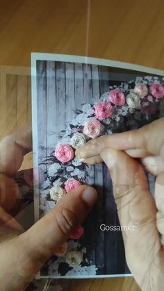 two hands touching each other over a photo with pink and white flowers on the table