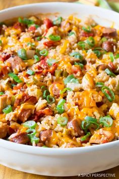 a casserole dish with sausage, rice and green onions in it on a wooden table