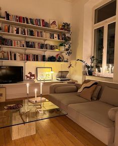 a living room filled with furniture and bookshelves next to a window covered in candles