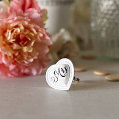 a white heart shaped ring sitting on top of a table next to flowers and coins