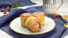 three cinnamon rolls on a plate next to a cup of coffee and spoon, with cinnamon sticks in the background