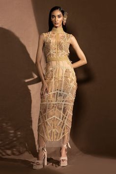 Dusk net fitted dress with high neck, embroidered gold metallic floral motifs and glass beads stripe pattern embellishment.
Component: 1
Pattern: Embellished and Embroidered
Type Of Work: Metallic Work and Glass Bead Cords
Neckline: High Neck
Sleeve Type: Sleeveless
Fabric: Net
Color: Beige
Other Details: 
Sheer illusion back
Back keyhole cut work button closure
Note: The headpiece and inner dress worn by the model is not for sale
Occasion: Cocktail,Party - Aza Fashions Gold Sleeveless Fitted Evening Dress, Luxury Gold Sleeveless Dress, Luxury Sleeveless Dresses With Sheer Bodice, Gold Sleeveless Evening Dress For Gala, Gold Summer Dress For Banquet, Gold Summer Evening Dress For Gala, Gold Summer Banquet Dress, Luxury Lace Sleeveless Evening Dress, Fitted Gold Embroidered Evening Dress For Party