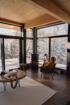 a woman sitting in a chair looking out the window at snow covered mountains and trees