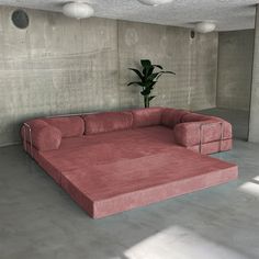 a large pink couch sitting in the middle of a room next to a potted plant