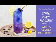 a blue and purple drink sitting on top of a wooden tray next to lemons