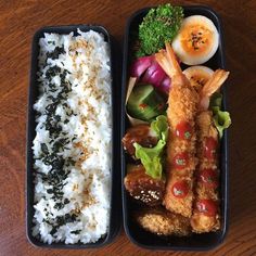 two black trays filled with food on top of a wooden table next to each other