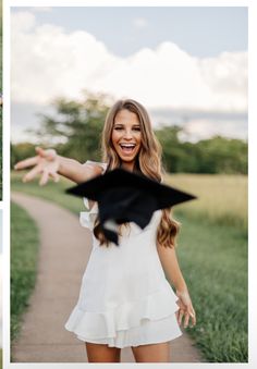 a woman in a white dress is throwing a black graduation cap into the air while standing on a path