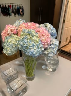 a vase filled with pink and blue flowers on top of a table next to two glasses