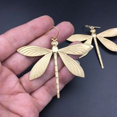 a pair of gold toned dragonfly earrings in the palm of someone's hand