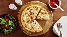 a pizza sitting on top of a wooden table next to a bowl of salad and utensils