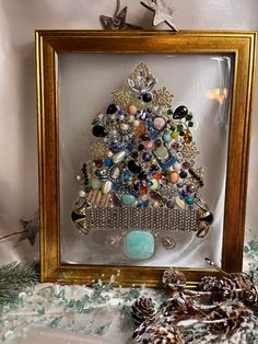 a christmas tree made out of beads and other items in a gold frame on a table