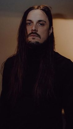 a man with long hair wearing a black turtle neck sweater