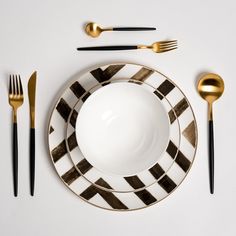 a white plate with black and gold stripes on it next to two forks, knives and spoons