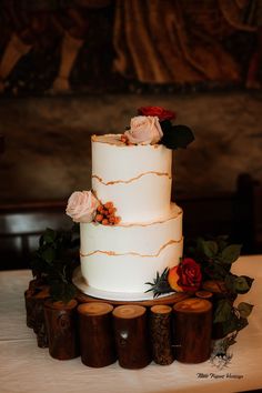 a three tiered white wedding cake with red and orange flowers on the top is surrounded by wood slices