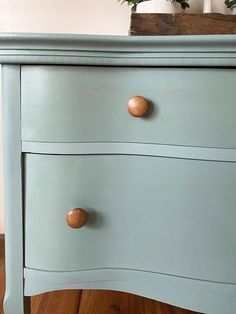 a blue dresser with wooden knobs on it's drawers and wood flooring