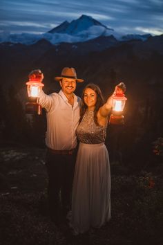 a man and woman holding two lanterns in front of a mountain at night with the lights on