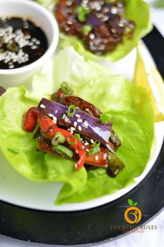 lettuce wraps filled with vegetables and sauce on a white plate next to a small bowl of dipping sauce