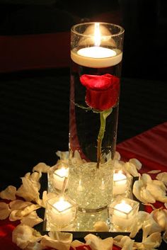 a candle and some flowers in a vase on a red table cloth with candles around it