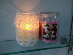 a lit candle sitting on top of a glass shelf next to a crocheted jar