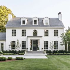 a large white house with lots of windows on the front and side of it, surrounded by lush green grass