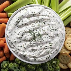 a dip in a bowl surrounded by vegetables and crackers on a platter with carrots