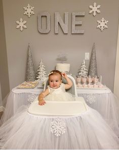 a baby sitting in a high chair at a cake table with snowflakes on it