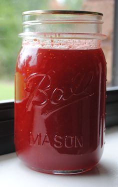 a mason jar filled with red liquid sitting on top of a window sill