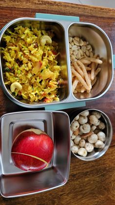 three metal containers filled with food sitting on top of a wooden table next to an apple